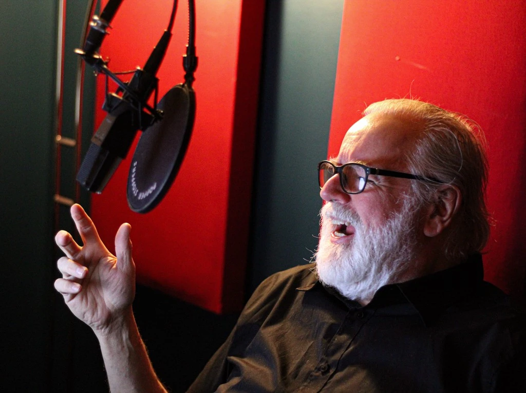 Glenn doing voiceover in front of a mic with red background